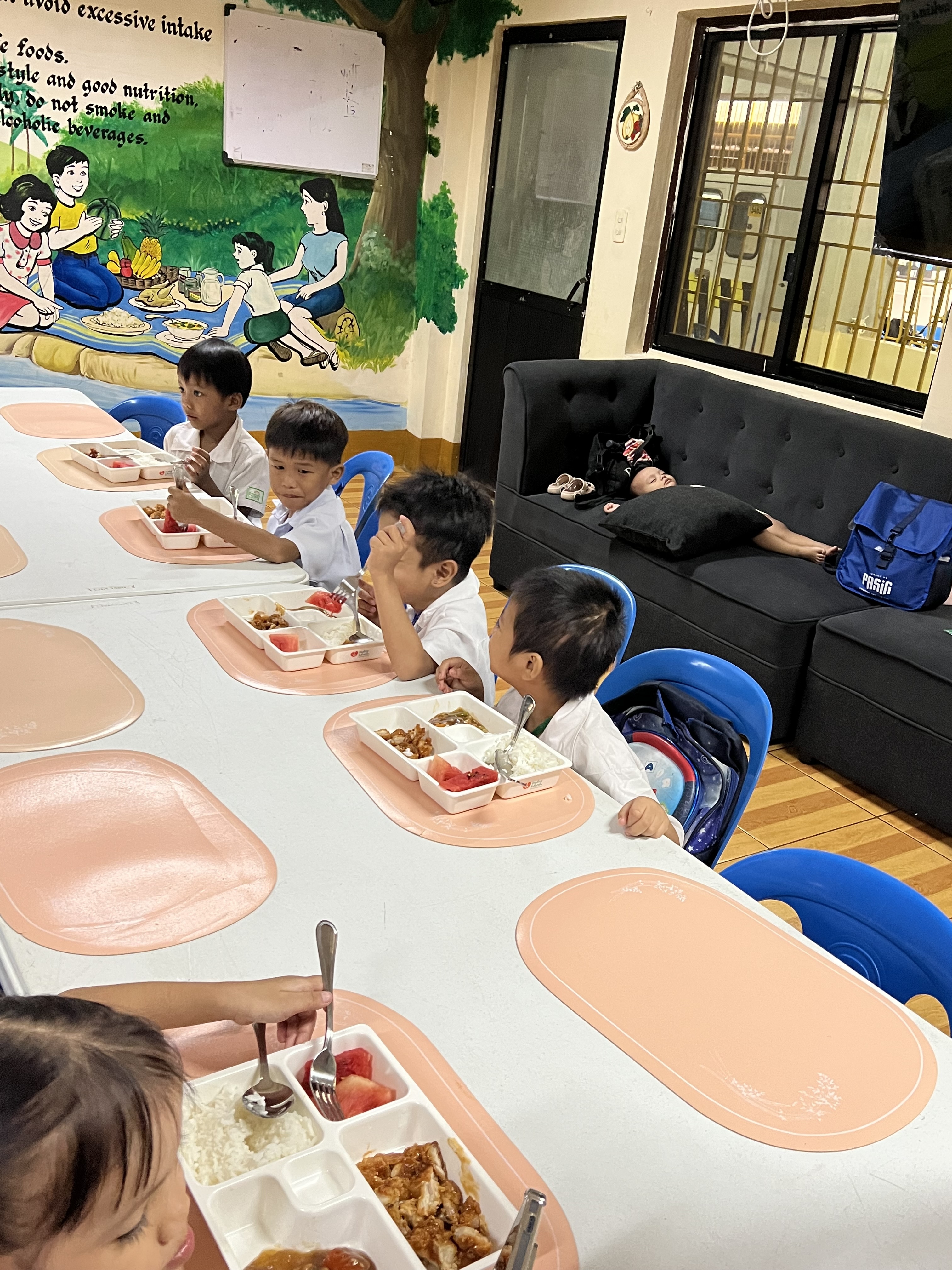 A long table of children in school uniforms eating their complete meals.