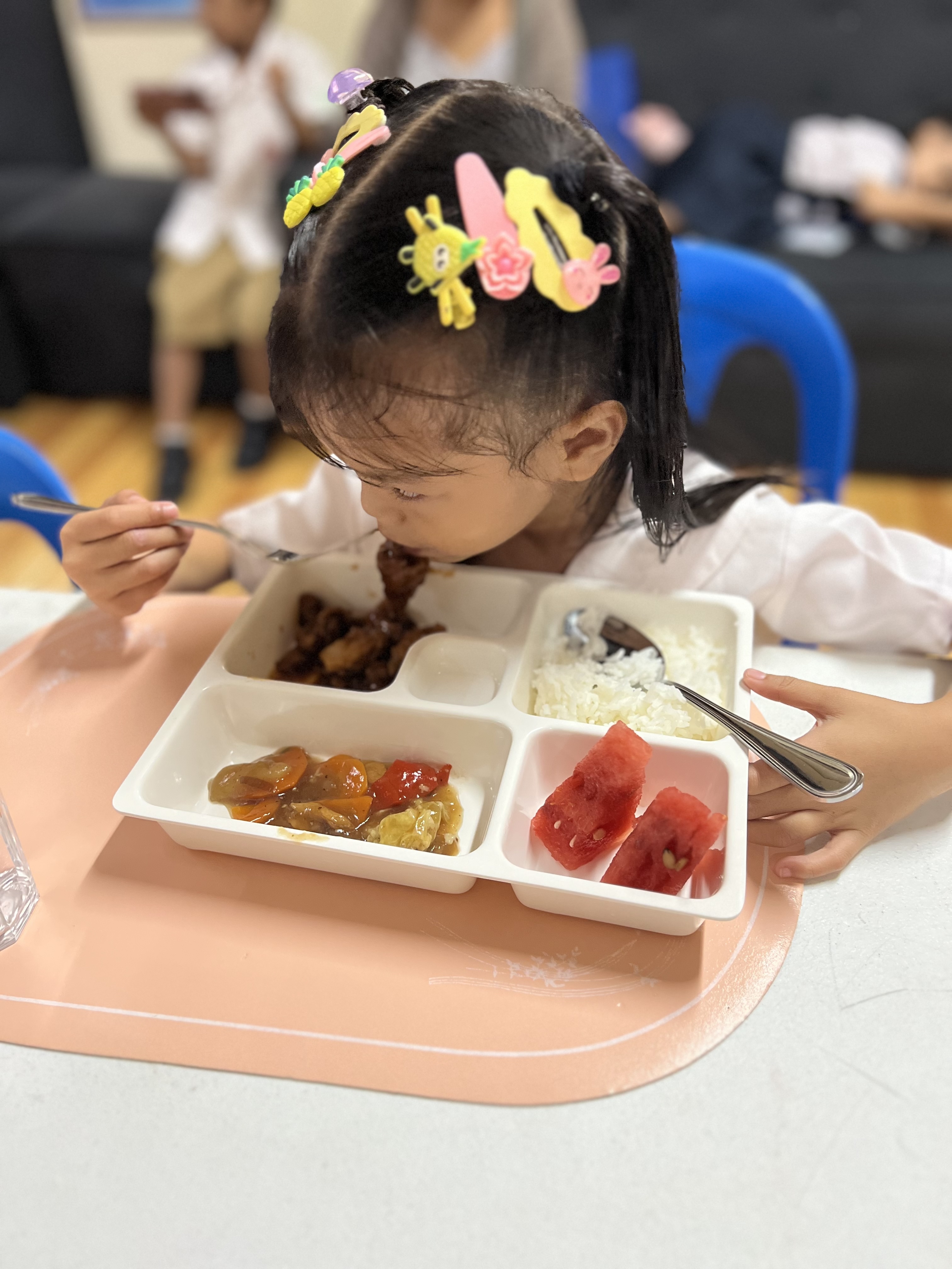 A young girl with colorful hair clips focused on eating her meal.