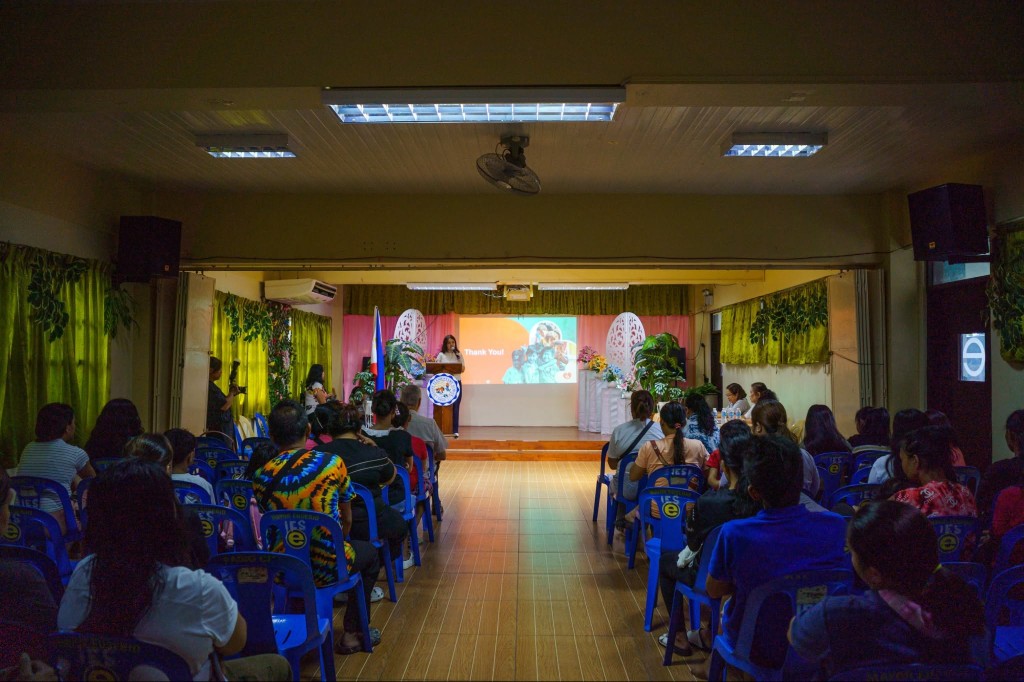 A speaker addresses the audience from a podium as a Thank You slide is shown on screen at the kickoff program.