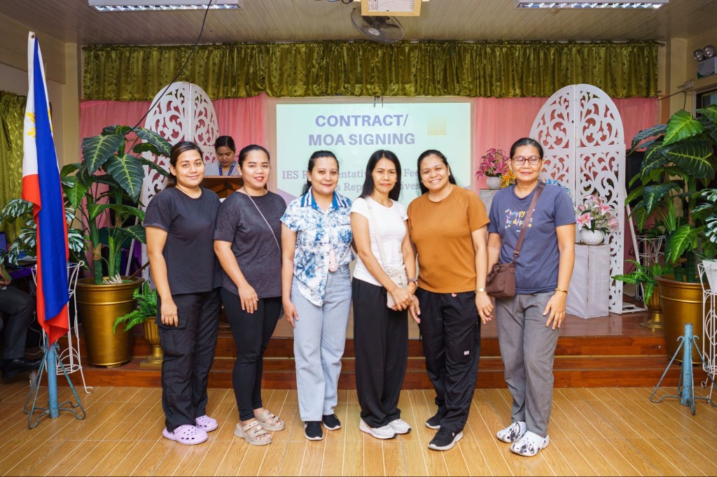 Six representatives from Ilugin Elementary School and Feeding Futures PH standing on stage in front of a Contract / MOA Signing slide.